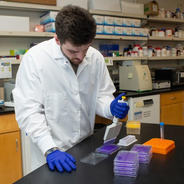 A student in a white coat dispenses liquid into a container